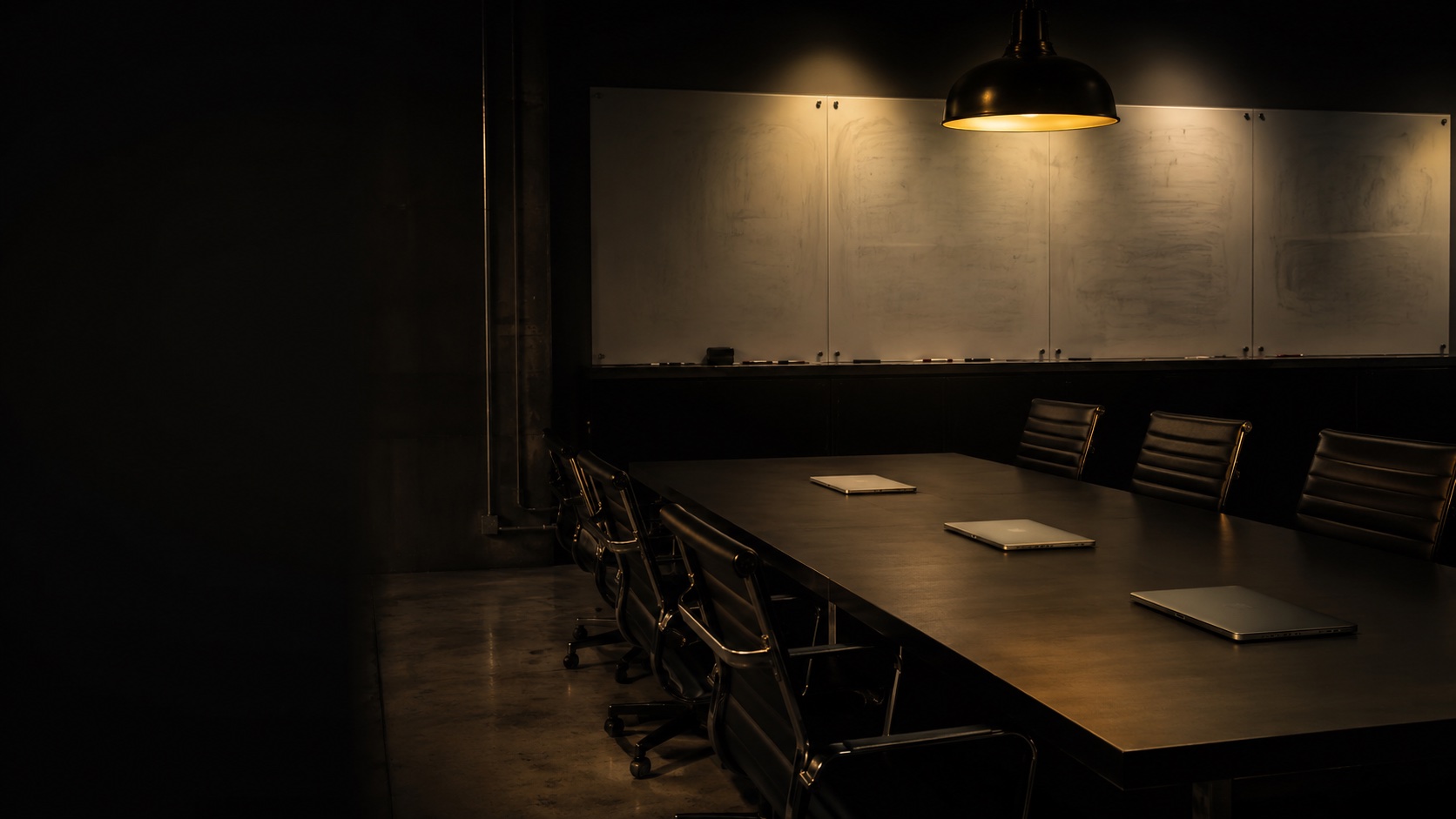 Empty conference room with three closed laptops and whiteboards under a single amber pendant